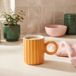 Single orange ceramic mug with vertical ridges and a round handle, interior is white, on a white background. - view 1