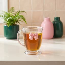 Clear glass mug with a handle and a small, solid light pink bow attached to the front, on a white background. - view 1