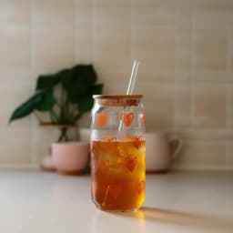 Clear glass can-shaped cup with orange heart outlines, bamboo lid, and clear glass straw on white background. - view 1