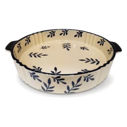 Round cream porcelain baking dish with dark blue leaf patterns and fluted edges, featuring two small handles on a white back… - view 2