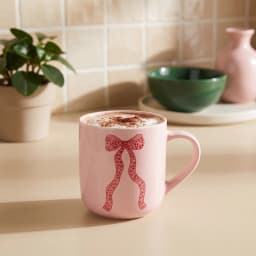 Single light pink ceramic mug with a red polka dot ribbon design on a white background, showing the handle. - view 1